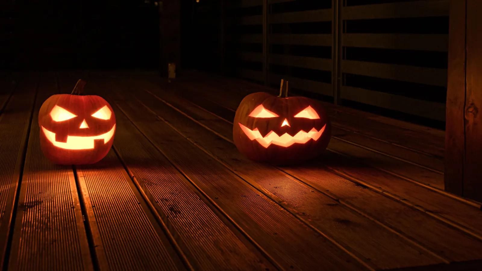 Seasonal atmosphere: two carved jack-o'-lanterns glowing on a wooden deck at night (stock photo)